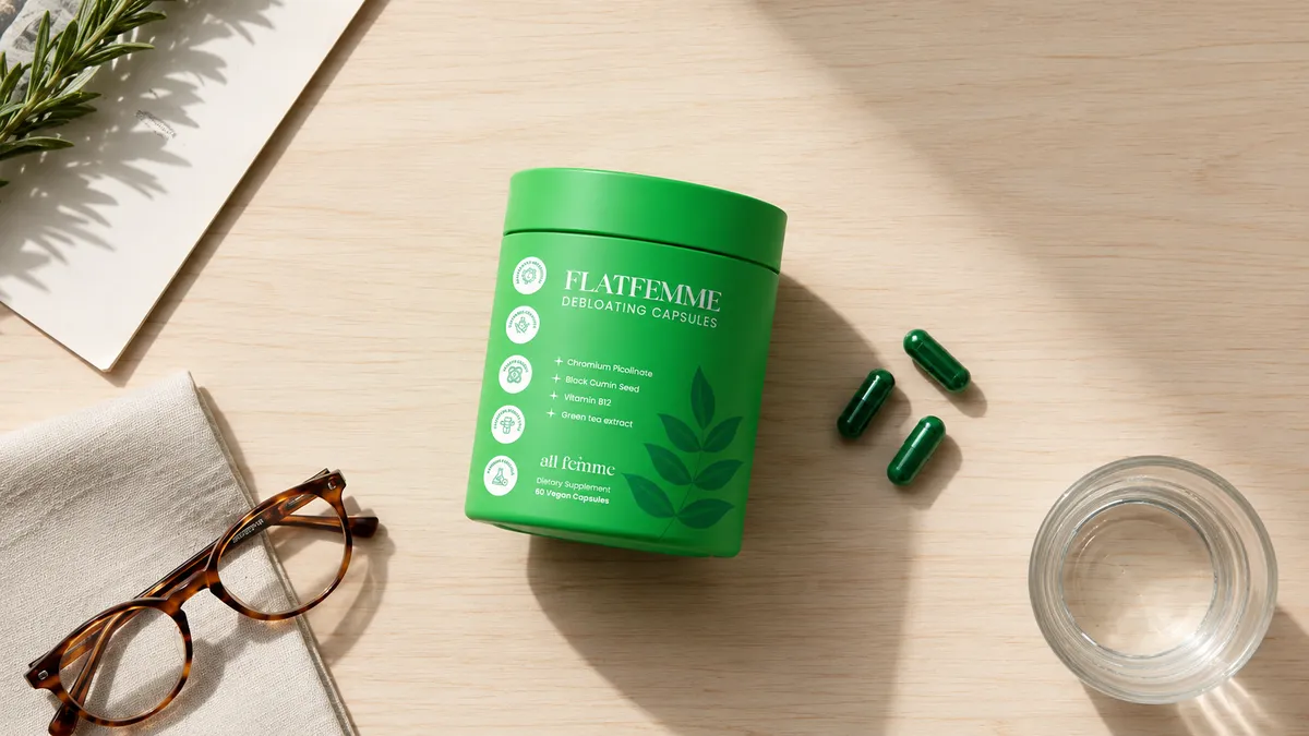 The green FlatFemme jar and capsules arranged on a desk with reading glasses and water
